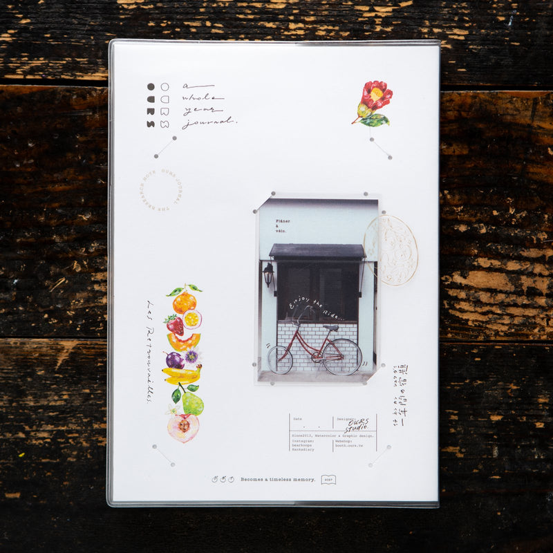 OURS Studio 2027 journal, The Reunion, with the shopfront and bicycle minicard in its cover slot. Photo: OURS Studio