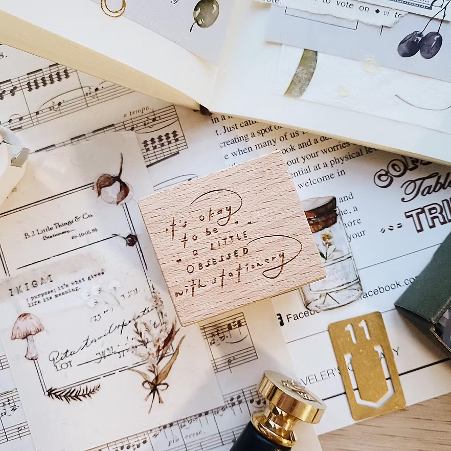 Close-up flatlay with a wooden 'obsessed with stationery' stamp, sheet music and dried flowers